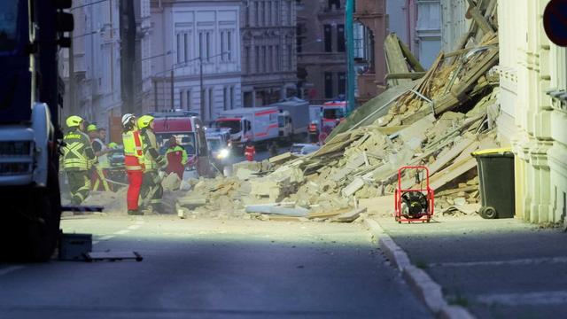 Feuerwehrleute stehen vor einem eingestürzten Haus.