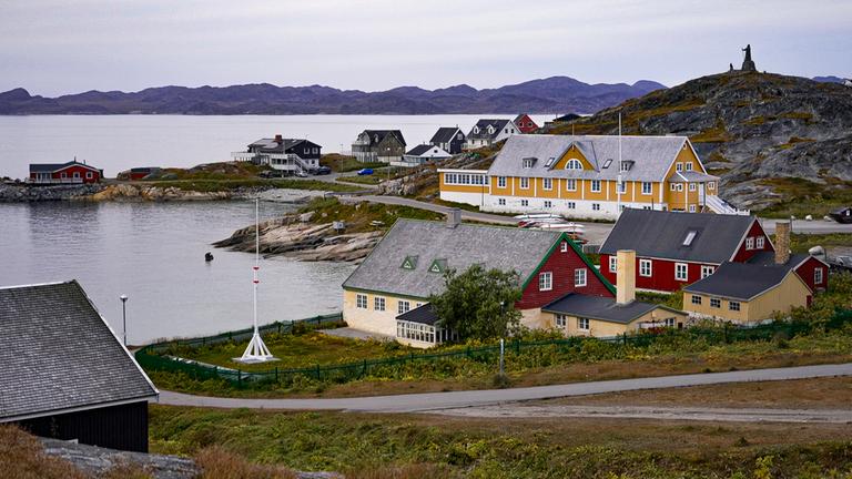 Auf einem Berg hinter Häusern einem Ufer steht ein Denkmal.