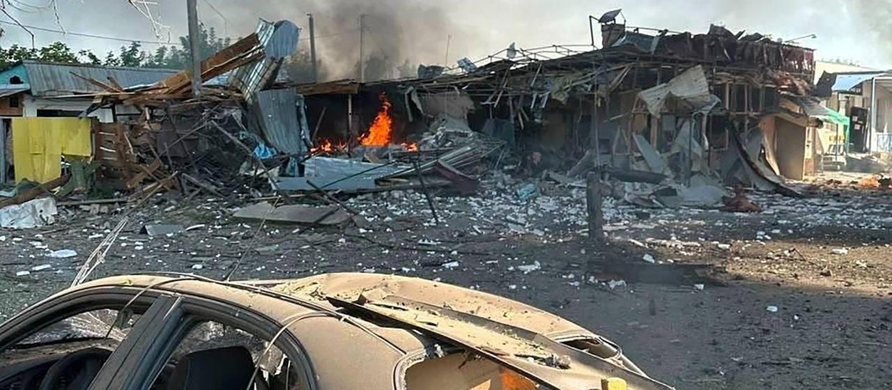 Ein zerstörtes Auto neben einem brennenden Gebäude nach einem Luftangriff in Petschenihy in der Region Charkiw in der Ukraine.