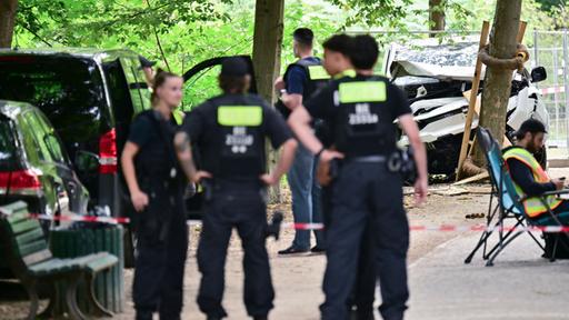 Polizisten stehen vor einem zerstörten weißen Fahrzeug im Bereich des Tiergartens.