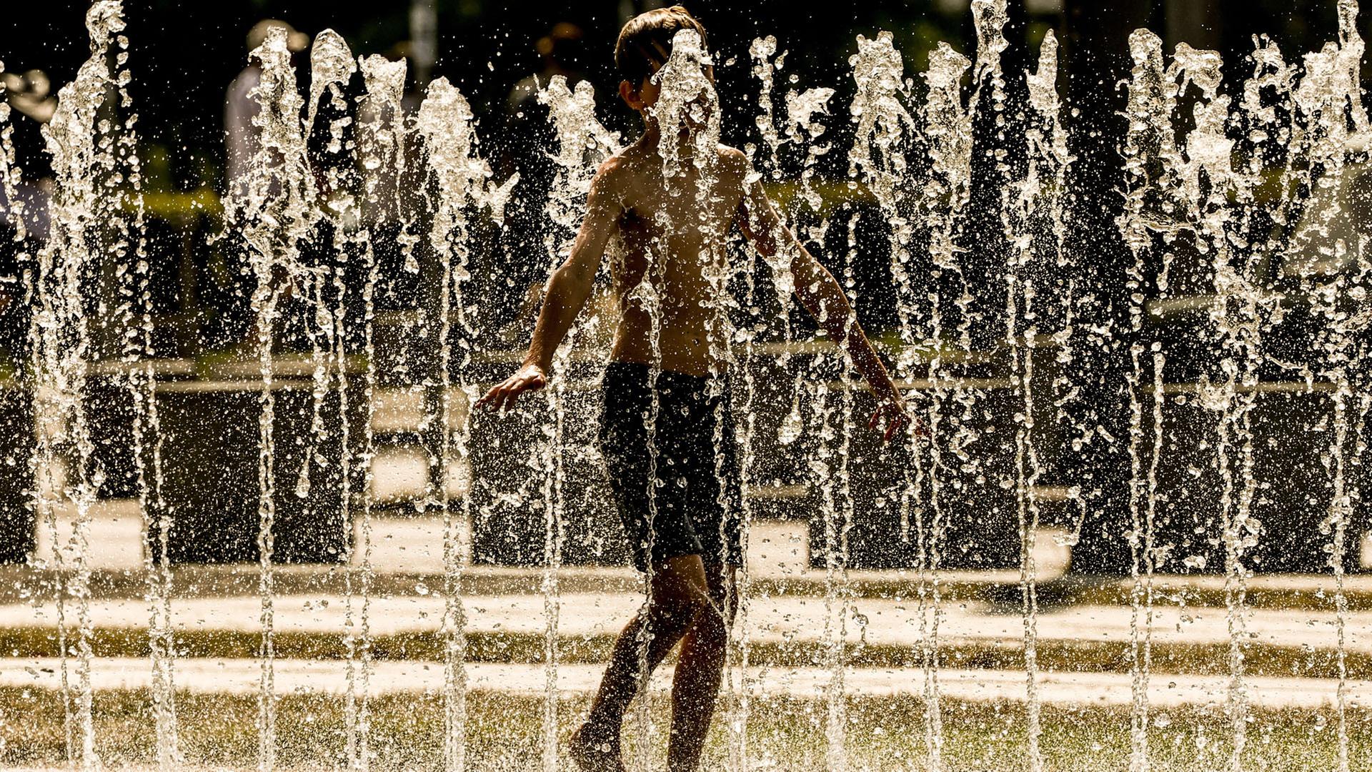 Ein junger Mensch kühlt sich an einem öffentlichen Brunnen im Regierungsviertel von Berlin ab. | EPA