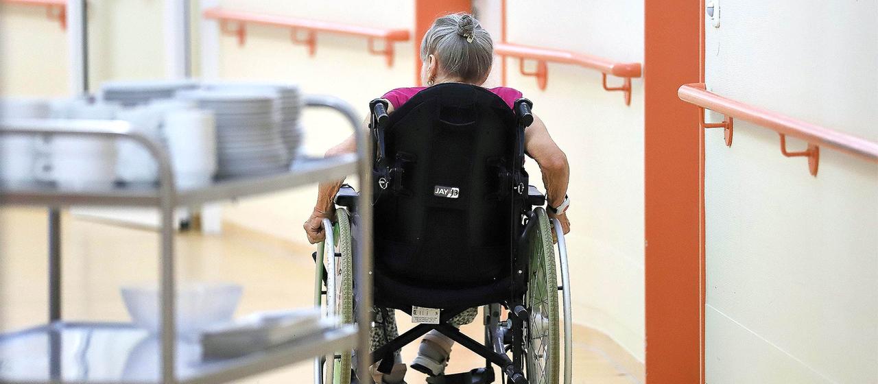 Eine alte Frau fährt in einem Rollstuhl durch ein Pflegeheim.