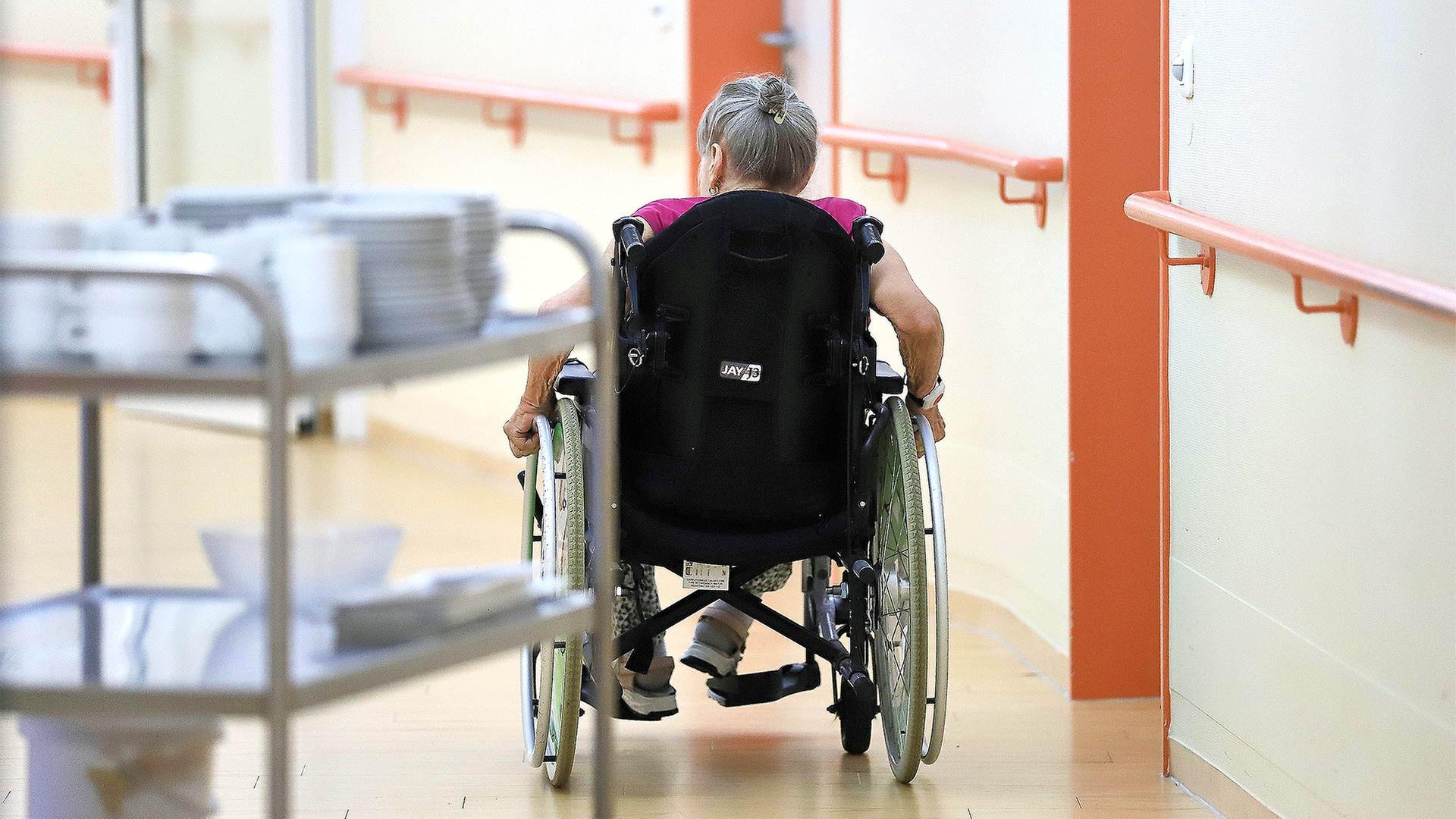 Eine alte Frau fährt in einem Rollstuhl durch ein Pflegeheim. | picture alliance / dts-Agentur