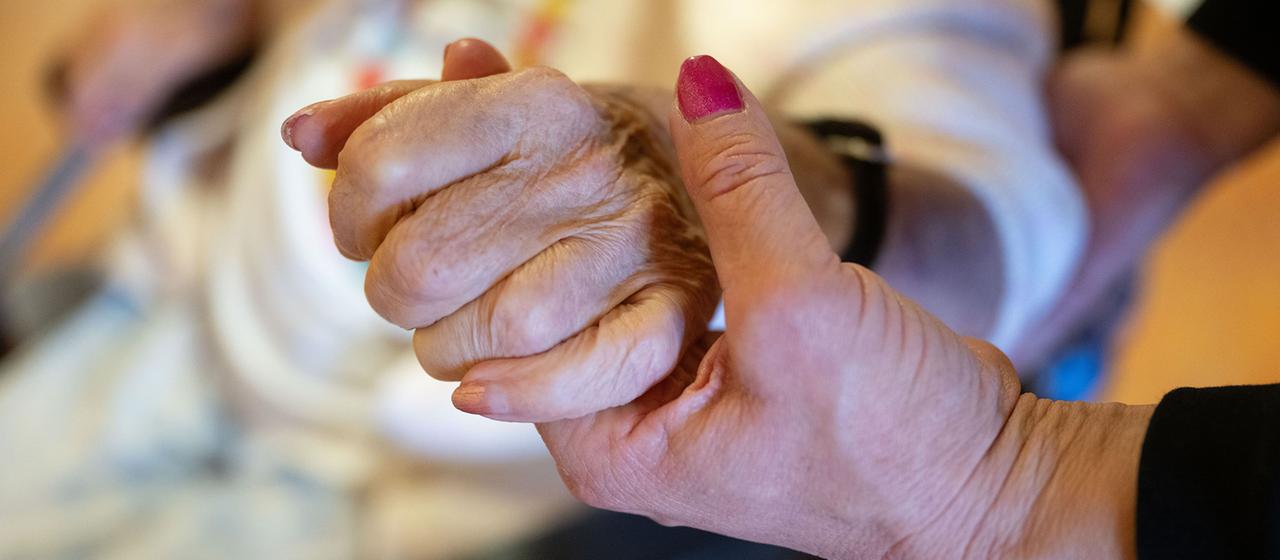 Eine Physiotherapeutin hält die Hand einer Pflegebedürftigen.