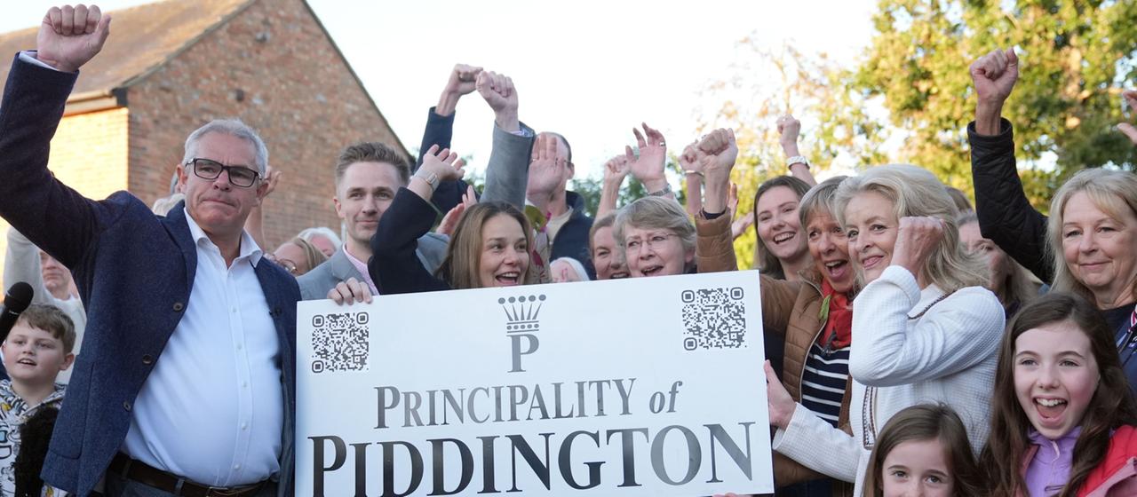 Anwohner posieren vor einem Schild mit der Aufschrift "Fürstentum Piddington".