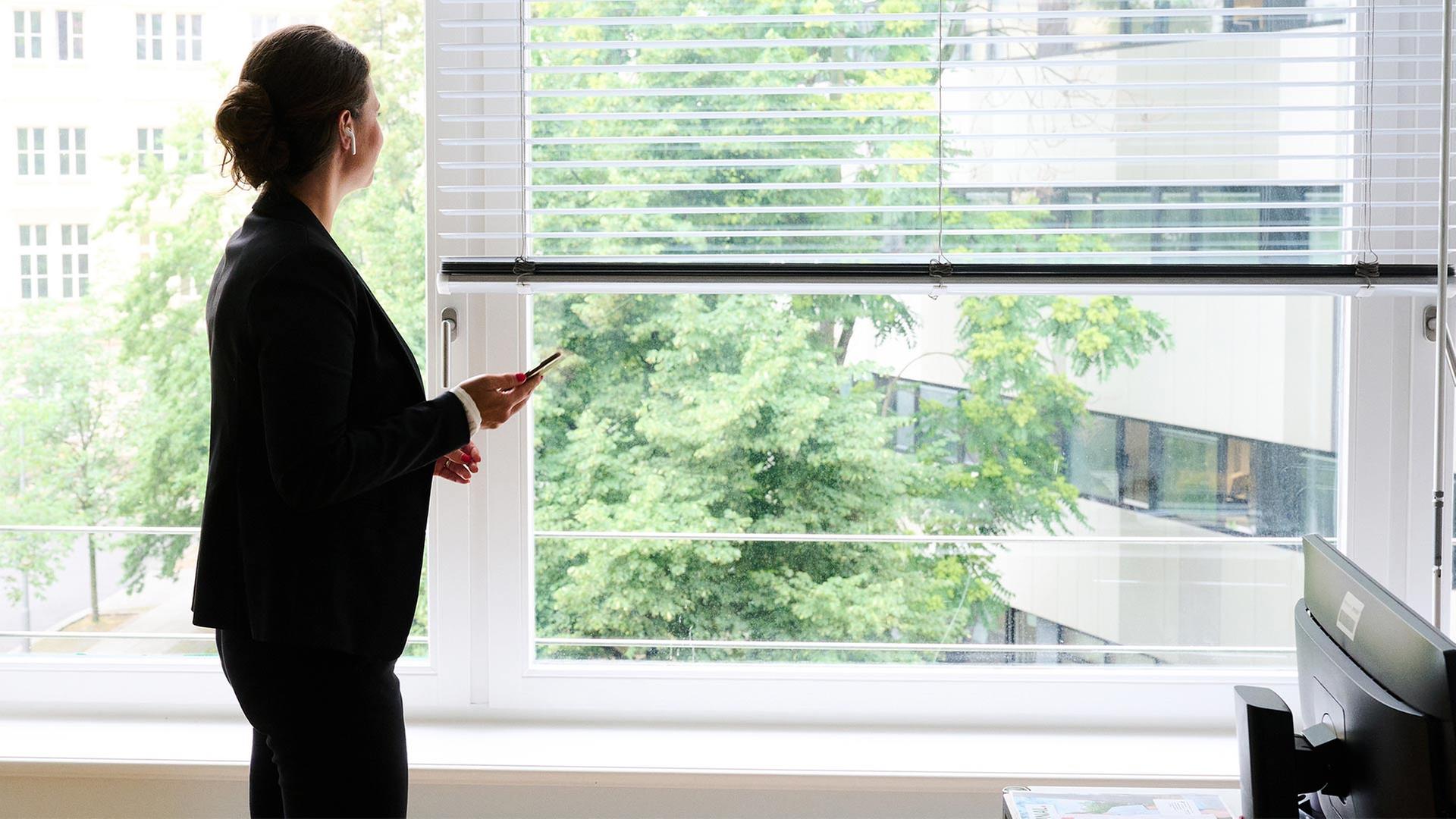 Eine Frau steht in einem BÃ¼ro am Fenster und telefoniert. | picture alliance/dpa