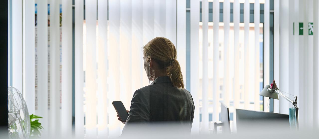 Eine Frau steht in einem Bürozimmer am Fenster und telefoniert über ein Headset.