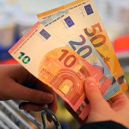 Eine Frau mit einem Einkaufswagen hält Euroscheine in der Hand.