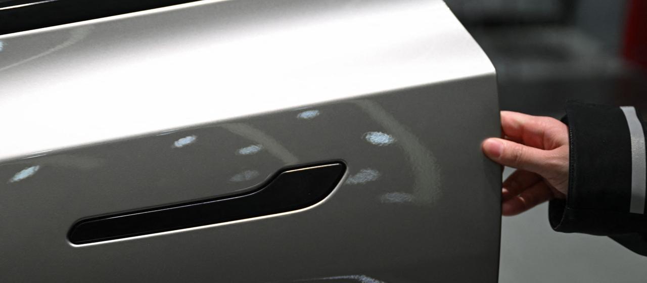 Eine Frau öffnet in einem Showroom in Peking die Tür eines Elektrofahrzeugs vom Typ Tesla Model YL.