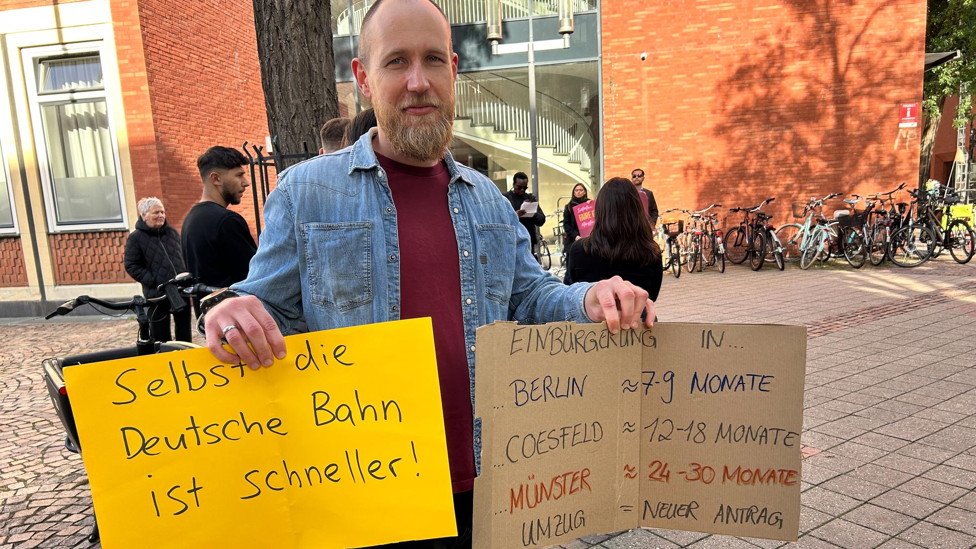 Ein Mann hält zwei Plakate hoch. | WDR/Helen Erdbrügge