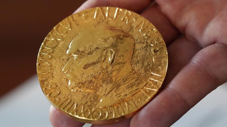 Eine Hand hält die Medaille des Friedensnobelpreises.
