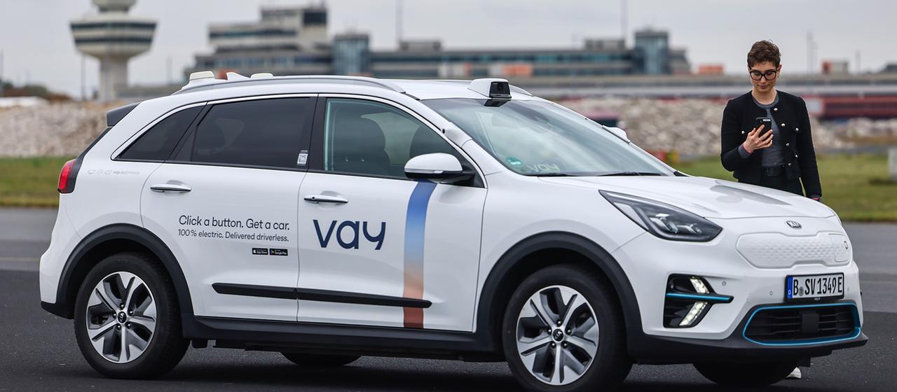 Eine Frau steht mit ihrem Smartphone in der Hand neben einem Auto.