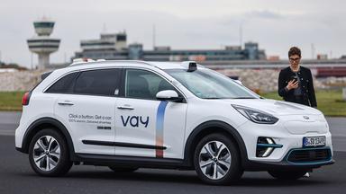 Eine Frau steht mit ihrem Smartphone in der Hand neben einem Auto.