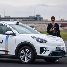 Eine Frau steht mit ihrem Smartphone in der Hand neben einem Auto.