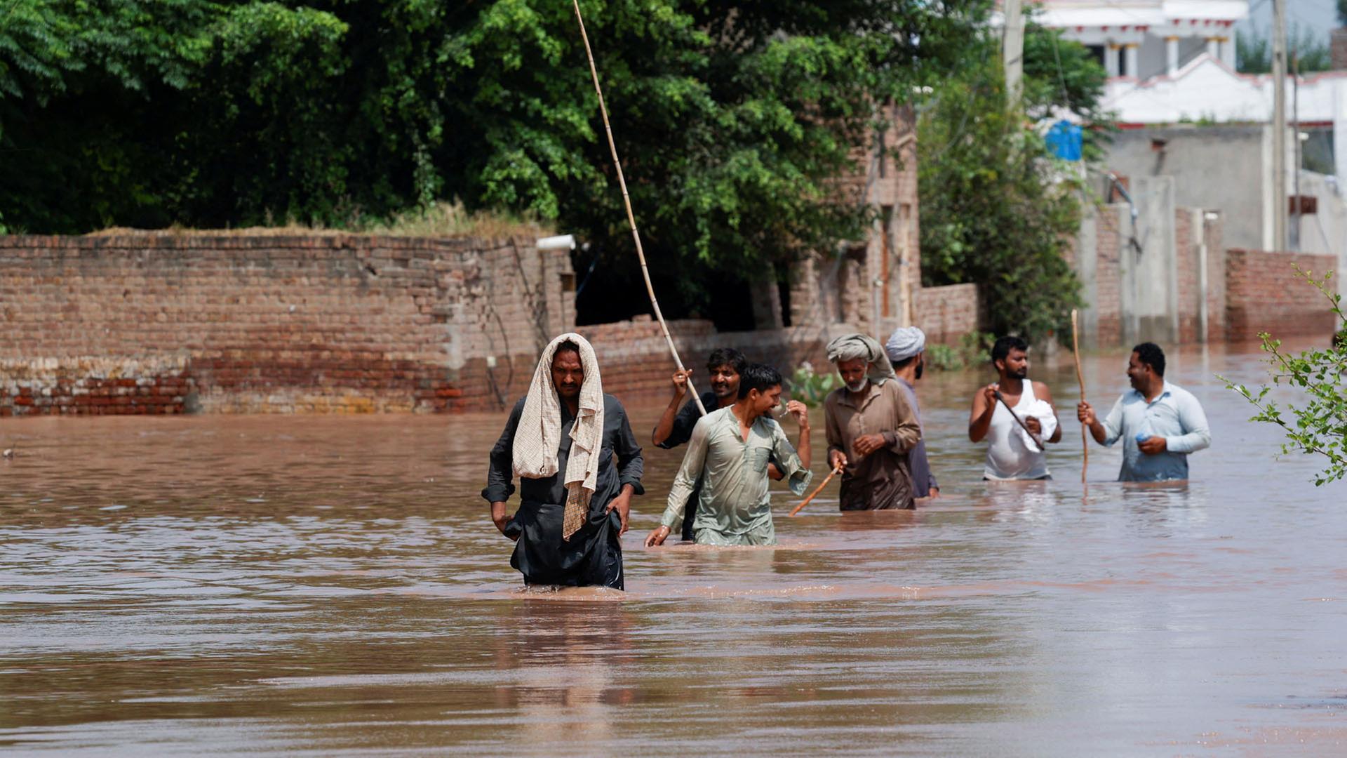 Anwohner waten durch eine überflutete Straße nach Monsunregenfällen und steigenden Wasserständen im Dorf Qadirabad, Pakistan. | REUTERS