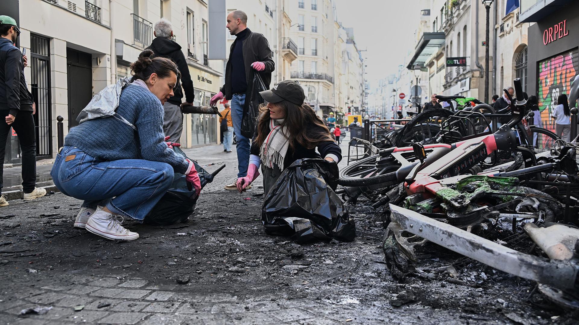  Menschen räumen auf einer Straße neben ausgebrannten Fahrrädern Trümmer weg. | Emma Da Silva/AP/dpa