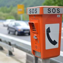 Auf einer vierspurigen Bundesstraße fahren mehrere Autos. Im Vordergrund des Bildes ist eine orangefarbene Notrufsäule zu sehen, auf der oben "SOS" steht.