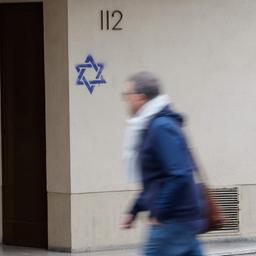Ein Mann geht in Paris an einem Gebäude entlang, dessen Fassade nachts mit Davidsternen beschmiert wurde. 