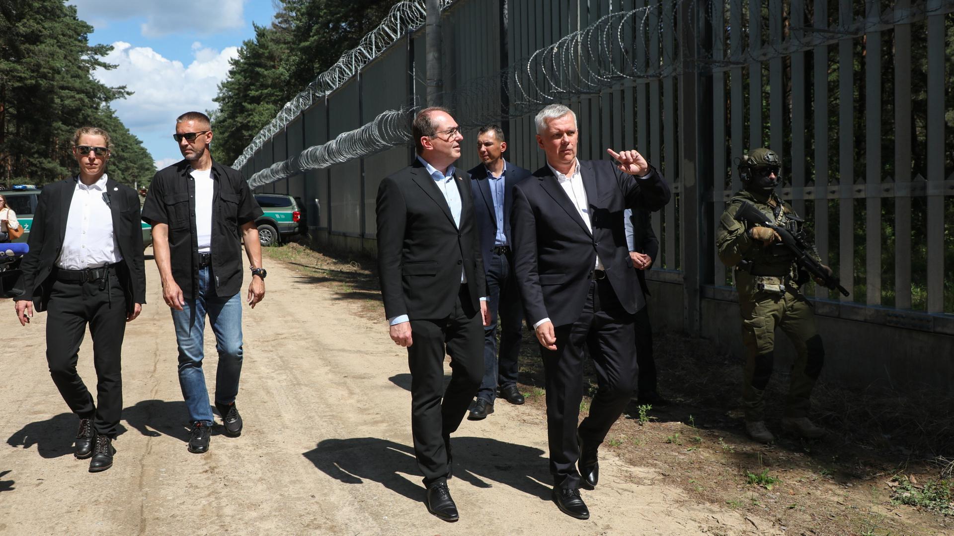 Tomasz Siemoniak (Mitte rechts) und Alexander Dobrindt gehen am Grenzzaun an der polnisch-belarusischen Grenze entlang. | dpa