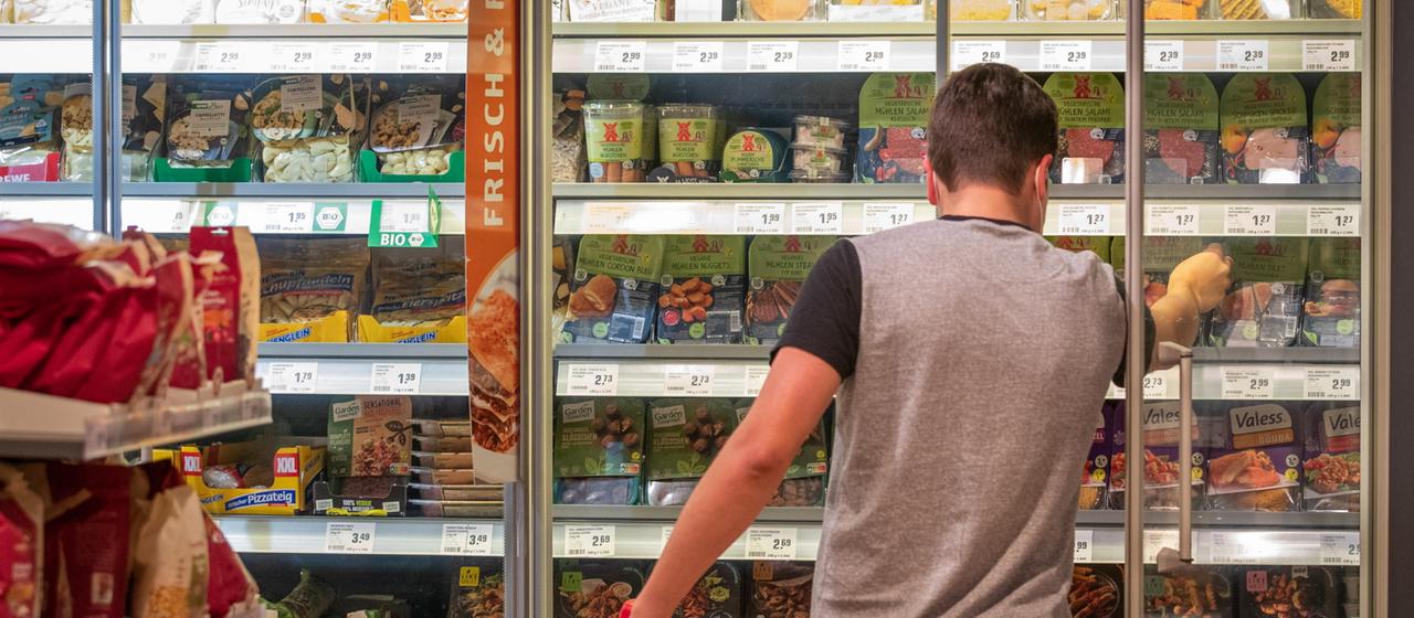Ein Mann greift in einem Supermarkt zu Fleischersatzprodukten.