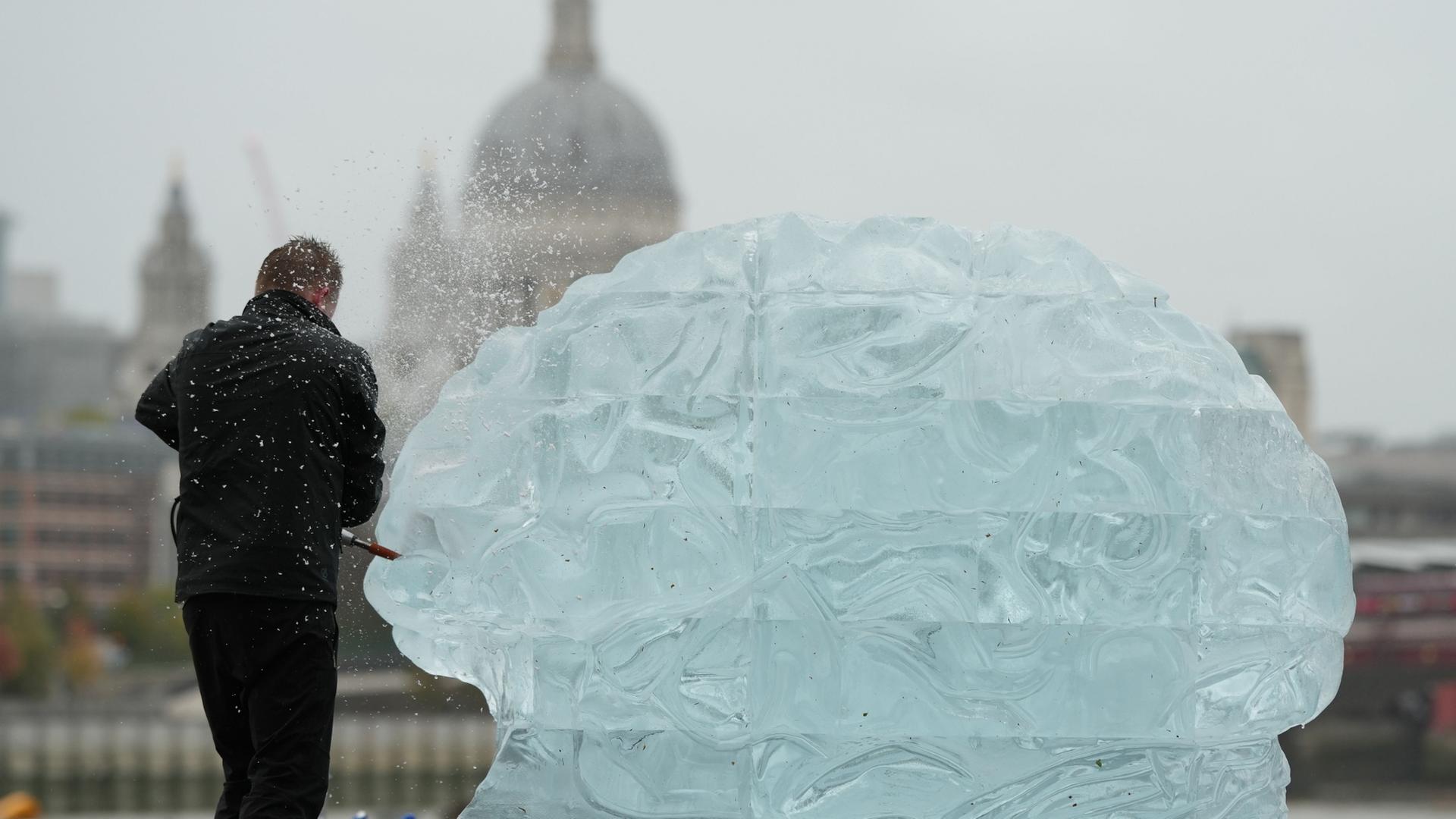 Eine Person arbeitet an einer Eisskulptur, die das menschliche Gehirn darstellt. | AP Photo/Alastair Grant