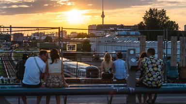 Menschen schauen sich auf der Modersohnbrücke den Sonnenuntergang hinter dem Fernsehturm an.
