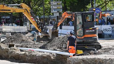 Ein Arbeiter steht in der Münchener Innenstadt auf einer Baustelle an einem Bagger.