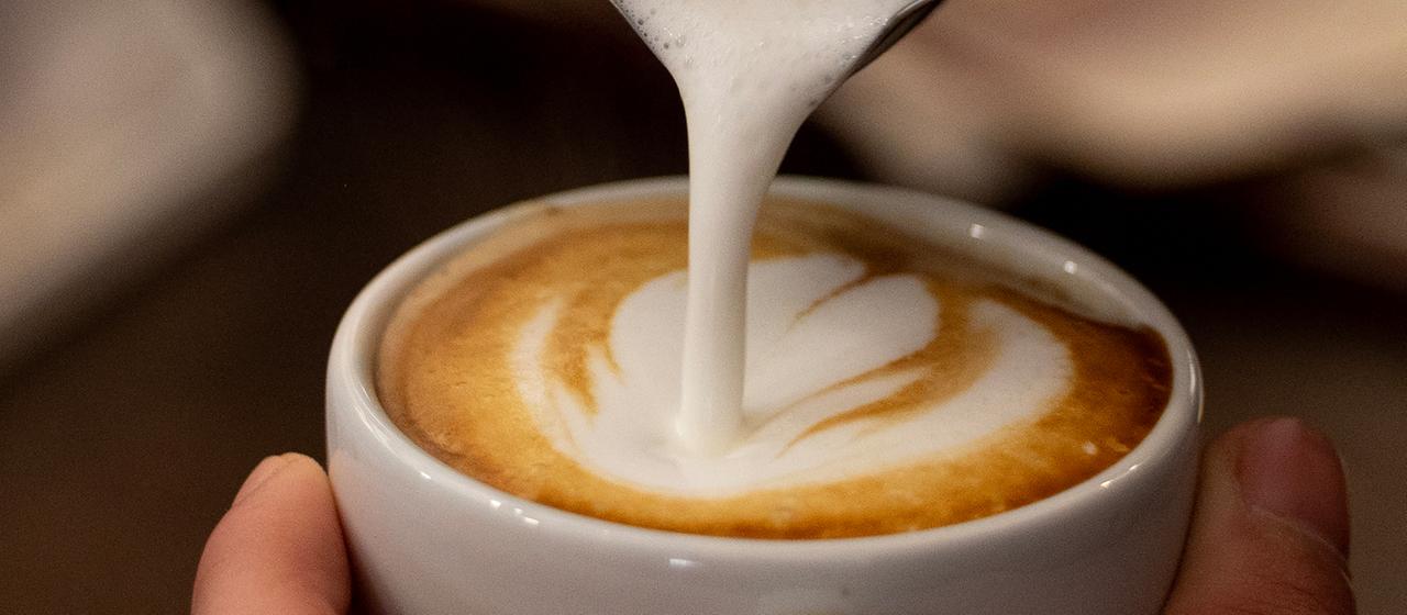 Milch wird in eine Tasse Kaffee gegossen.