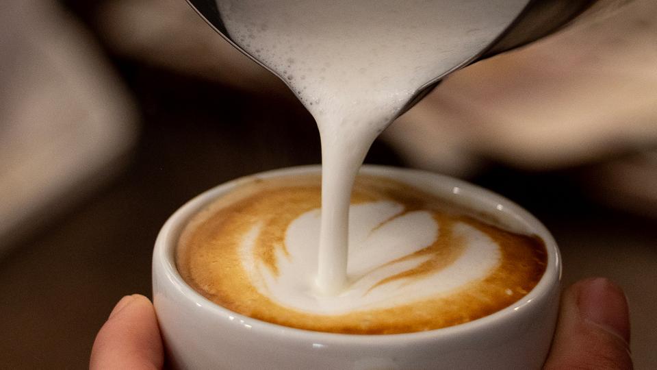 Milch wird in eine Tasse Kaffee gegossen.