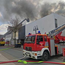 Zwei Feuerwehrfahrzeuge stehen mit ausgefahrenen Drehleitern auf einer Straße. Auf den Leitern stehen Feuerwehrleute und löschen.
