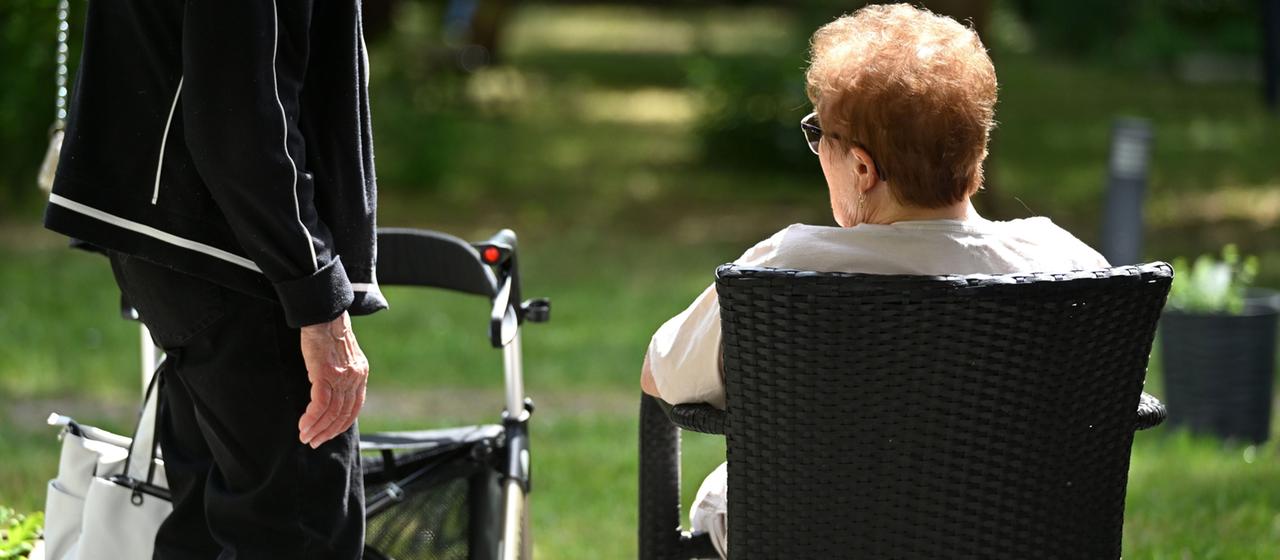 Zwei Senioren sprechen in dem Garten eines Pflegeheims miteinander.