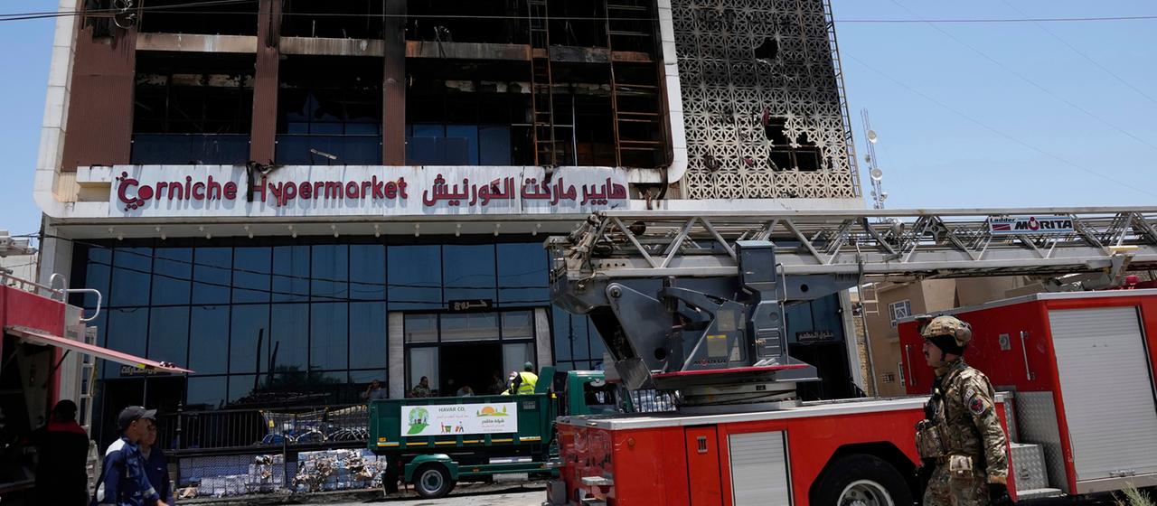 Feuerwehrleute stehen vor einem ausgebrannten Supermarktgebäude in Al-Kut, Irak. 