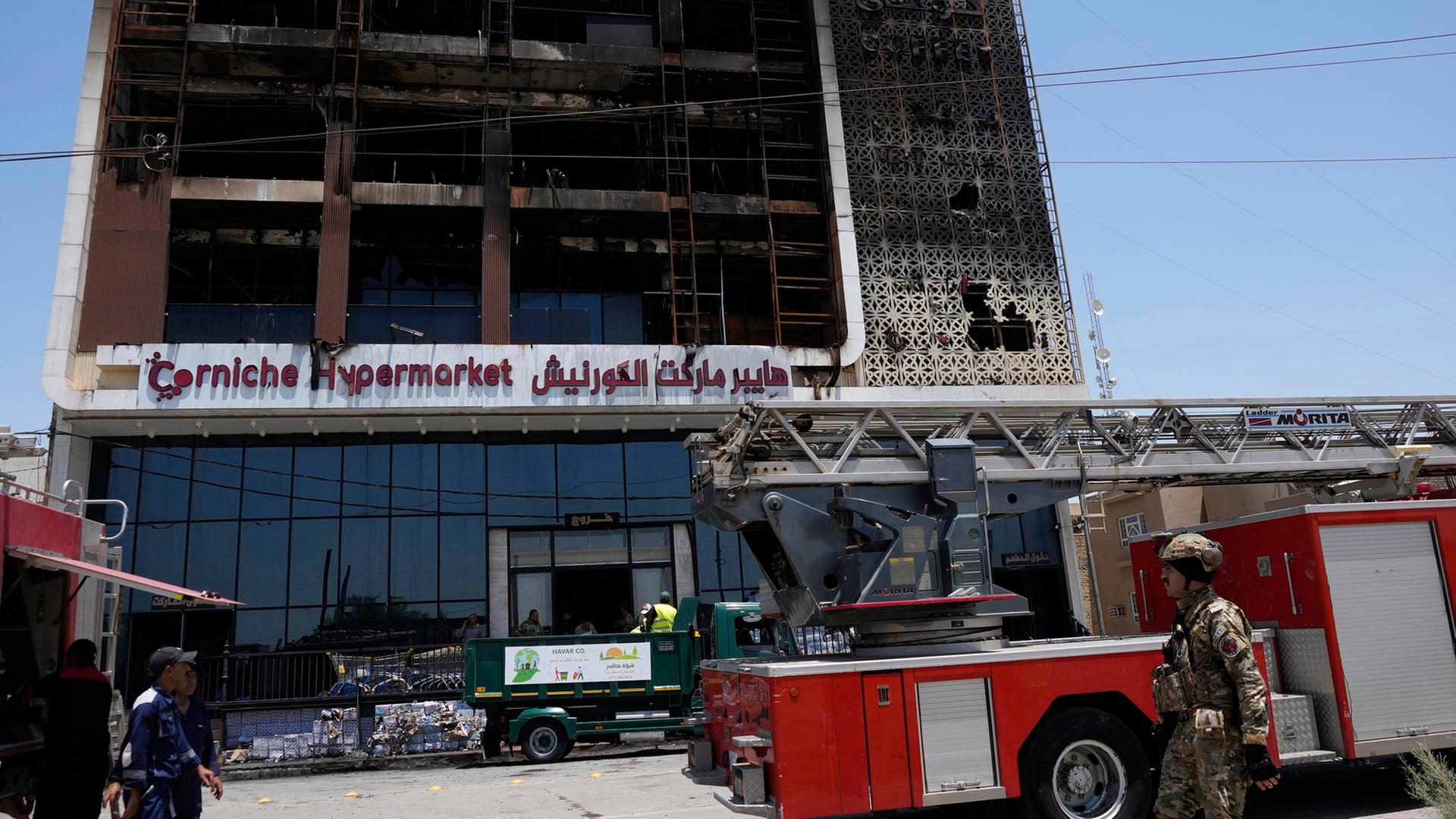 Feuerwehrleute stehen vor einem ausgebrannten Supermarktgebäude in Al-Kut, Irak.  | dpa