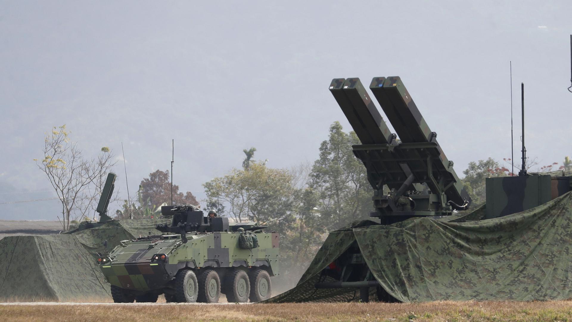 Ein Panzerfahrzeug fährt während einer militärischen Übung in Taichung County, Taiwan,  an einer Mehrfachraketenabschussvorrichtung vorbei. | ChiangYing-ying/AP/dpa