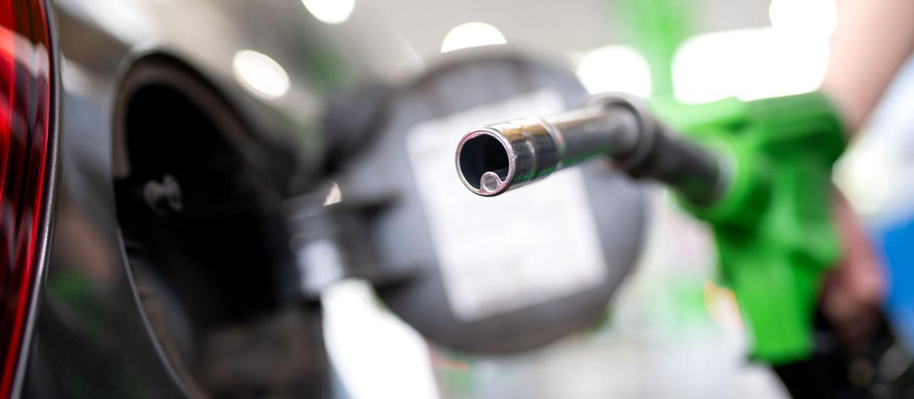 Eine Frau hält an einer Tankstelle an einer Zapfsäule eine Zapfpistole in der Hand.