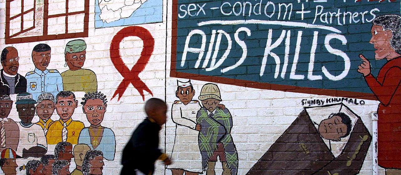 Ein Schuljunge rennt am 17.05.2002 in Soweto (Südafrika) an einem Wandbild vorbei, das vor Aids warnt.