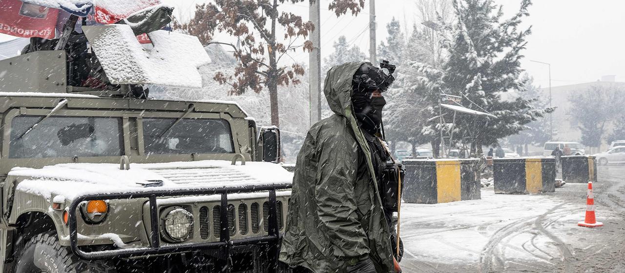 Ein bewaffneter Mann steht während Schneefalls an einem Kontrollpunkt Wache.