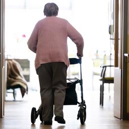 Eine Frau geht mit einem Rollator in einem Altenheim auf einem Gang entlang.