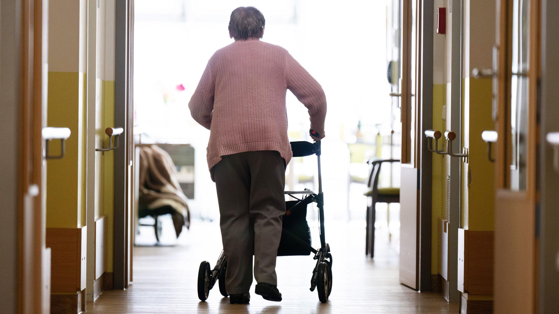 Eine Frau geht mit einem Rollator in einem Altenheim auf einem Gang entlang. | dpa