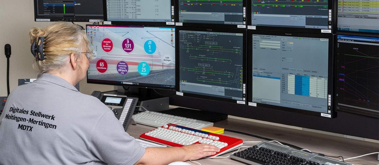 Eine Fahrdienstleiterin sitzt an Steuerbildschirmen eines digitalen Stellwerks.