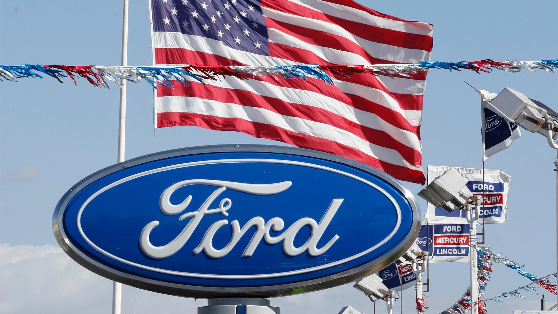 Ford Logo auf einem Schild und eine US-Flagge | picture alliance / ASSOCIATED PR