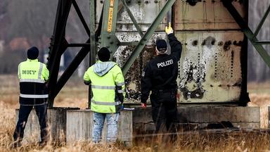 Ein Polizist und zwei Techniker untersuchen einen Strommast in der Nähe des Tesla-Werks in Brandenburg.