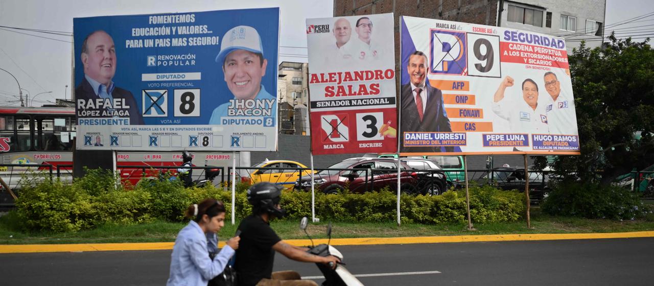Zwei Menschen auf einem Motorrad fahren in Lima an Wahlplakaten vorbei.