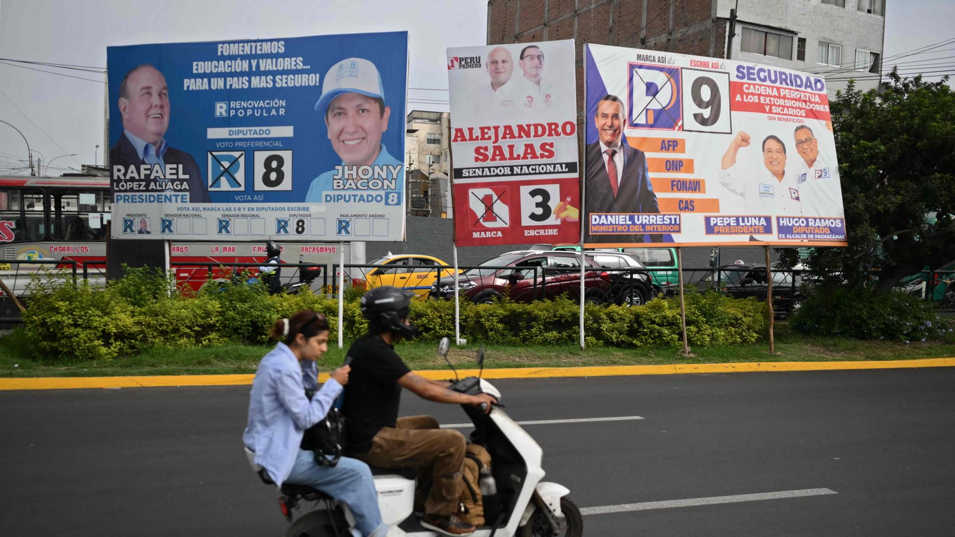 Zwei Menschen auf einem Motorrad fahren in Lima an Wahlplakaten vorbei. | AFP