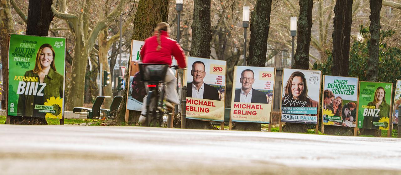 Eine Frau fährt mit einem Fahrrad an Wahlplakaten in Mainz vorbei.