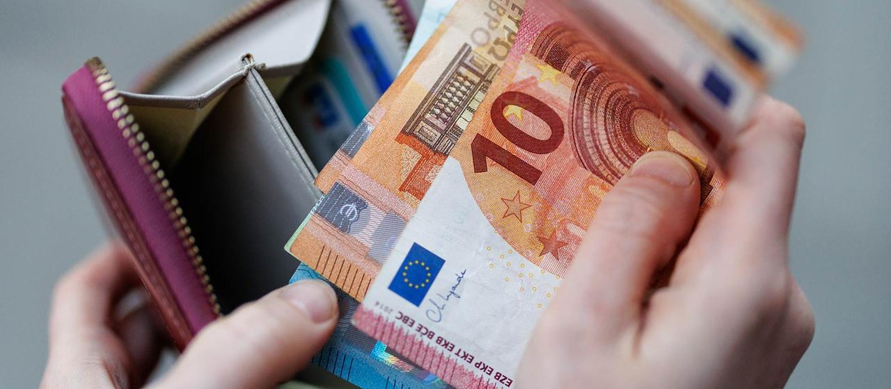 Eine Frau hält Geldscheine aus ihrem Portemonnaie in den Händen.