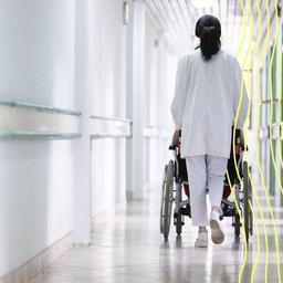 Ein Pfleger schiebt einen Patienten im Rollstuhl durch einen Krankenhausflur.