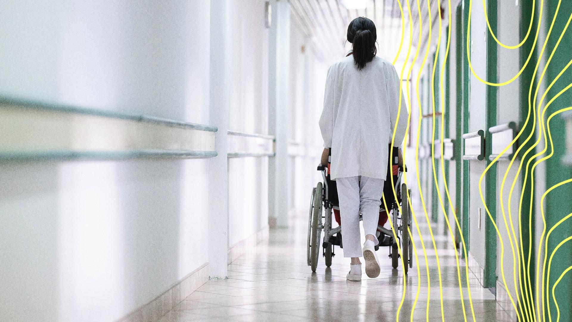 Ein Pfleger schiebt einen Patienten im Rollstuhl durch einen Krankenhausflur. | picture alliance / Zoonar | benis arapovic