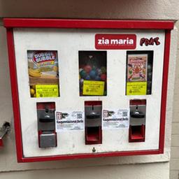 Ein Kaugummiautomat hängt an einer Hauswand.