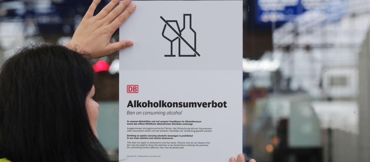 Eine Mitarbeiterin des Sicherheitsdienstes der Deutschen Bahn hält im Hauptbahnhof ein Plakat mit der Überschrift "Alkoholverbot" an eine Glaswand
